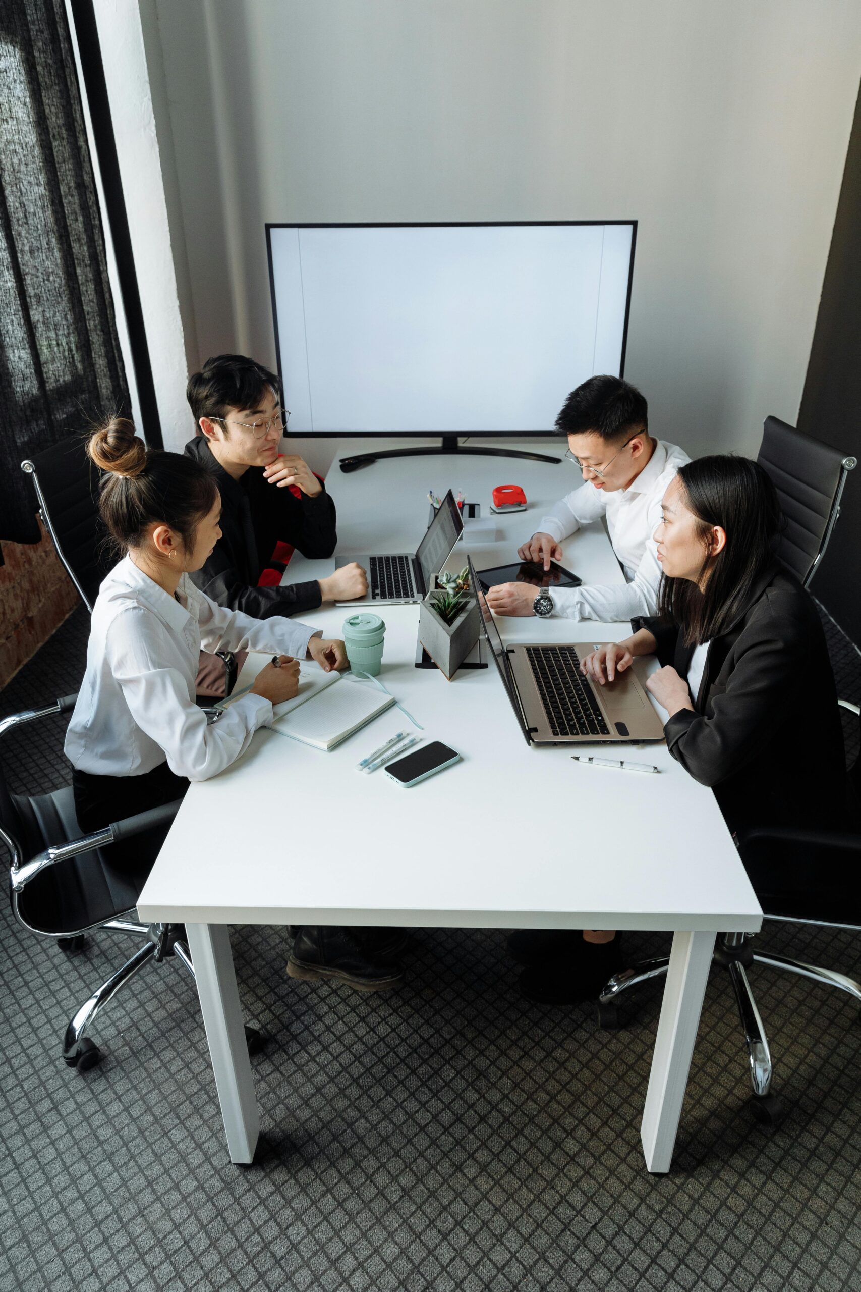 A group of professionals discussing a project in a modern office setting with laptops and a whiteboard.
